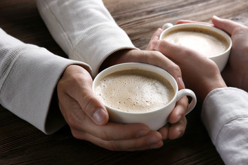 Lovely couple holding cup of coffee in hands on wooden background