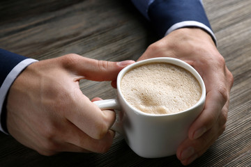 Man holding in hands cup of coffee on wooden background
