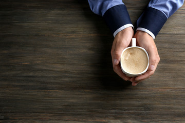 Man holding in hands cup of coffee on wooden background