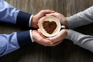 Lovely couple holding cup of coffee in hands on wooden background
