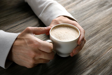 Man holding in hands cup of coffee on wooden background