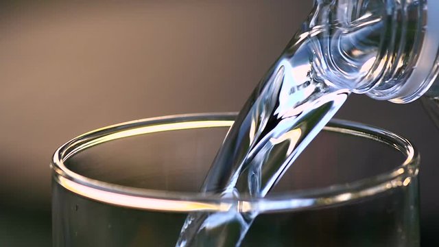 Drink water is pouring from bottle into glass below close up and slow motion shot
