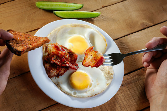 Eating fried eggs with bacon, sliced cucumber and bread