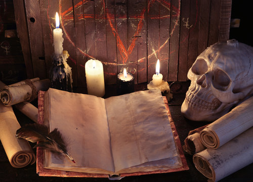 Open witch book with paper scrolls and evil candles against pentagram background