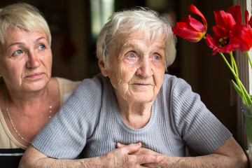 Pensive elderly woman portrait, with the adult daughter in the background.