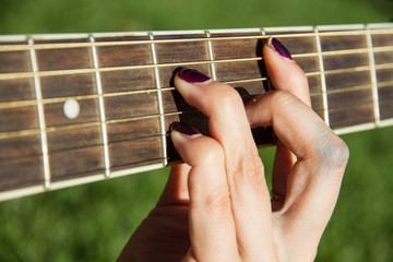 Girl playing guitar in the park in summer. The image is a close-up of hands making chords on the...