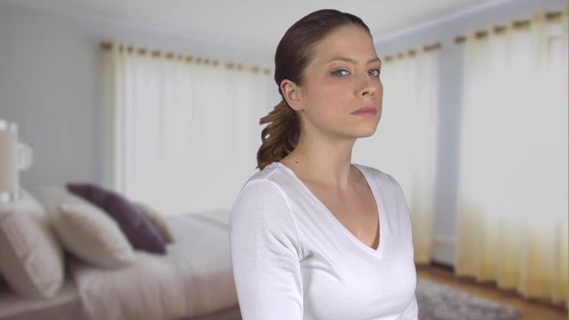 Woman turns and stares expressionless in bedroom