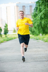 Running man jogging in city street park at beautiful summer day. Sport fitness model caucasian ethnicity training outdoor.