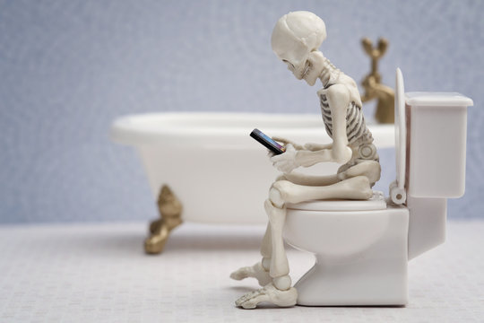 Skeleton sitting on water closet with his smartphone