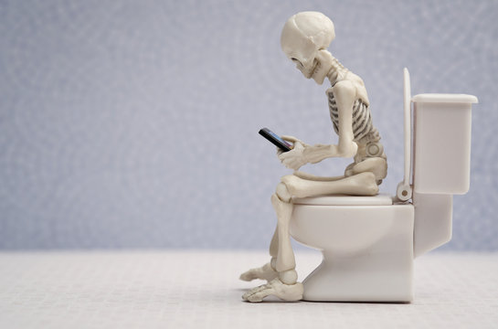 Skeleton sitting on water closet with his smartphone