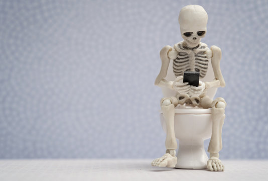 Skeleton sitting on water closet with his smartphone