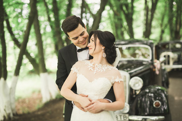 Happy newlywed couple, man and wife kissing near stylish retro car