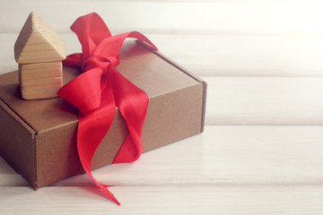 gift with a house/ gift wrapping of cardboard tied with a red ribbon with a model of a wooden house 