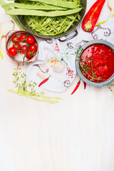 Green beans with tomatoes sauce, cooking  preparation on light wooden background with traditionally embroidered cloth and ingredients, top view, place for text