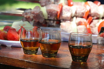 Three glasses of cognac on wooden table the background of raw kebabs threaded onto skewers