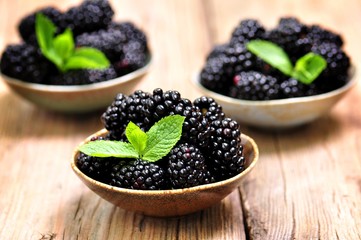 Organic blackberry with a mint leaf on a wooden background.