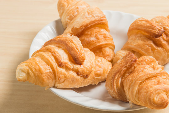 four gold croissant in white plate on wood table