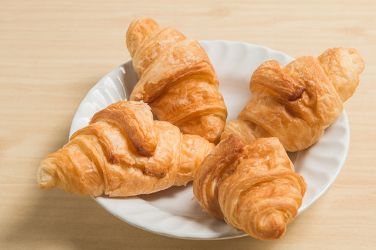 four gold croissant in white plate on wood table