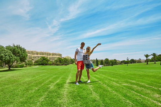 Young couple standing on a green field. Happy couple man and woman on the golf course. Blue sky and houses in the background.