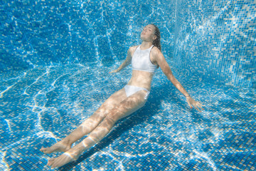 girl in the pool. She dives into the pool. Under water in a white bathing suit