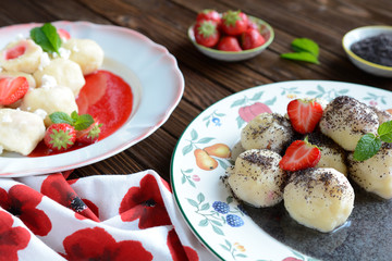 Two plates of  sweet boiled dumplings filled with strawberries with a poppy seed sauce and curd.