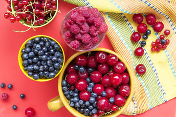 Summer fresh berries: blueberries, raspberries, cherries and redcurrent in bowls. Top view on a red and yellow background.