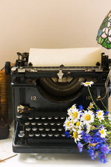 black vintage typewriter with books on wooden table with flowers