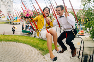 Emotional newlyweds screaming while riding on high carousel in amusement park. Expressive wedding couple at carnival.