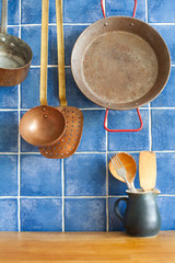 Vintage style kitchen accessories. Old utensils pan ladle pitcher with spoon, spatula. Wooden table and blue tile background. Kitchen interior