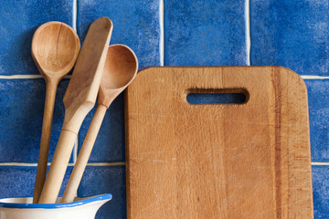 Cutting board, wooden spoons. Retro style, vintage kitchen utensils. Blue tile background. soft focus