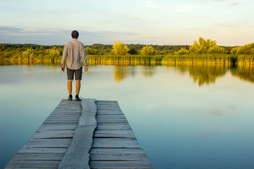 Fototapeta na wymiar Alone man standing on the edge of a pier on the lake