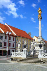 Plague column (Kuzno znamenje) at Main Square (Glavni Trg) of the city of Maribor in Slovenia, Europe. Historical center with religious sculpture. Street in the city and town. Bright sunny weather.