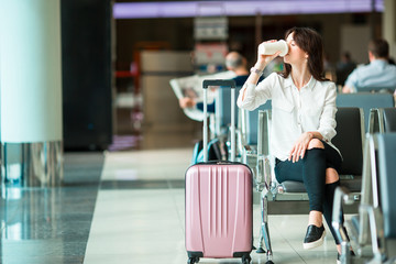 Airline passenger in an airport lounge drinking coffee and waiting for flight aircraft. Caucasian woman with glasss if hot coffee in the waiting room