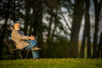 Fototapeta premium Portrait of a senior man outdoors, sitting on a bench in a park