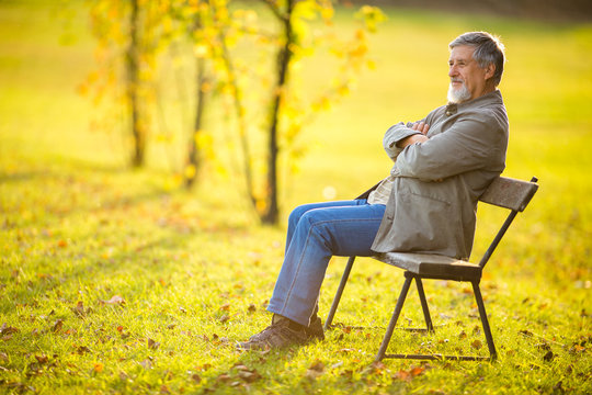 Portrait of a senior man outdoors, sitting on a bench in a park