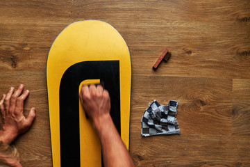 man rubs snowboard sponge wax on  wooden floor