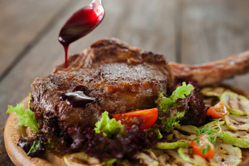 Rib steak showering with red sauce from teaspoon, closeup. Meat decor at restaurant