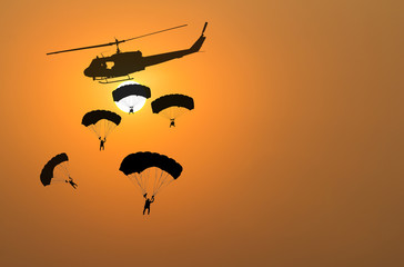 Silhouette of parachute and helicopter on sunset background