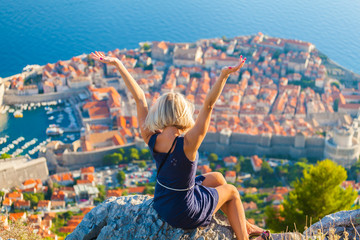 Young female traveler looks to the old city and sea from mountain in Dubrovnik. Summer vacation in...