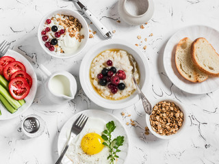 Assortment of breakfast - oatmeal with berries, fried egg, fresh vegetables, cottage cheese, yogurt and berries, homemade granola on a light table. Healthy food. Top view