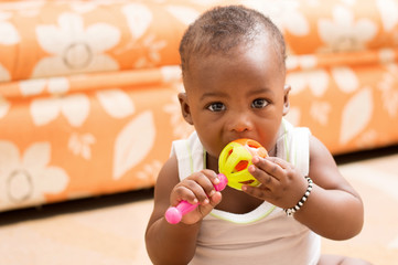 portrait d'un bébé assis portant à la bouche son jouet