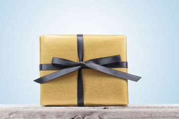 Golden wrapped gift box with black ribbon on a wooden table isol