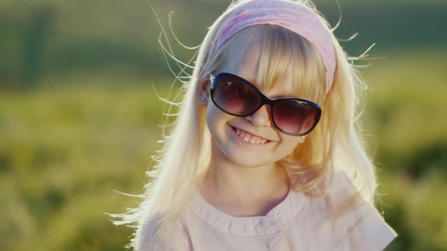 Blonde girl in sunglasses smiling at the camera. Sunny day in front of the sunset