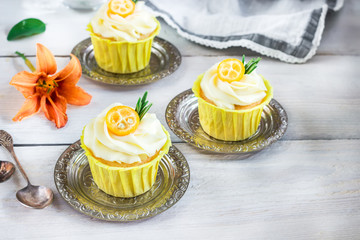 Cupcakes with cream cheese on white wooden table.