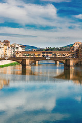 Obraz premium Ponte Santa Trinita bridge over the Arno River with cloudy sky and reflections, Florence, Italy