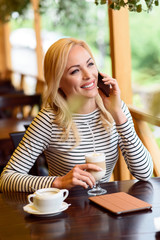 Joyful blond girl using telephone in cafe