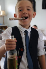 A smart dressed young boy pretending to smoke a cigar and drink a beer