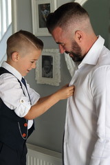 Obraz premium A young boy dressing his father on his wedding day as part of his best man duties