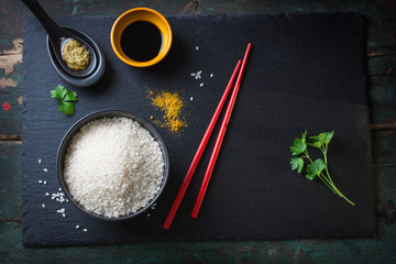 Composition with asian food - rice for sushi, spices, sauces and chopsticks on a wooden and stone background, top view