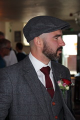 A groom at his wedding with a floral button hole and wearing a flat cap, 2016